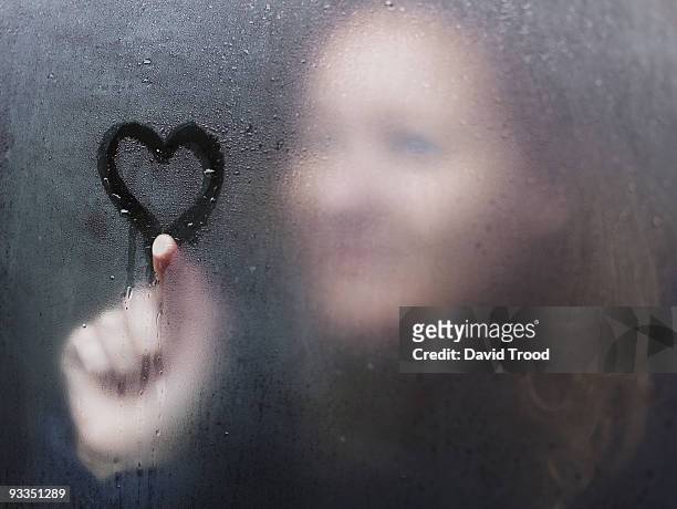 woman drawing a heart on window on a rainy day. - david trood stock-fotos und bilder