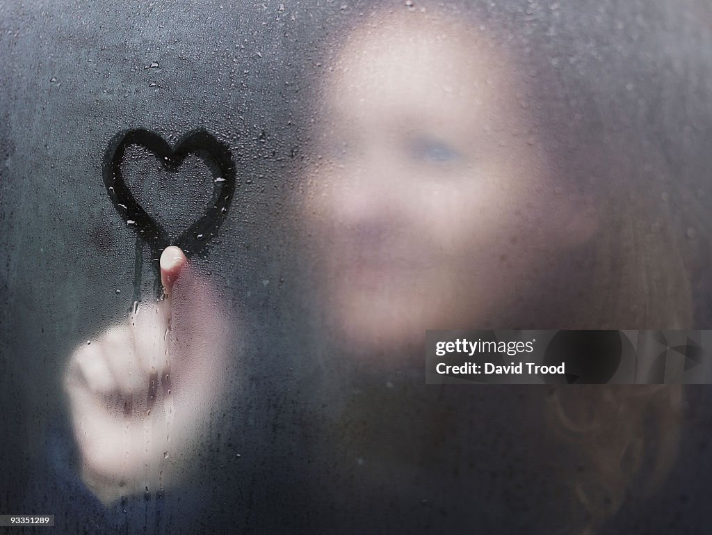 Woman drawing a heart on window on a rainy day.