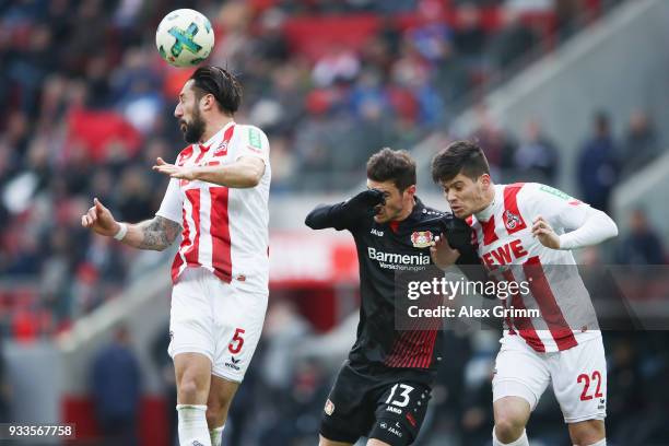 Lucas Alario of Leverkusen jumps for a header with Dominic Maroh and Jorge Mere of Koeln during the Bundesliga match between 1. FC Koeln and Bayer 04...