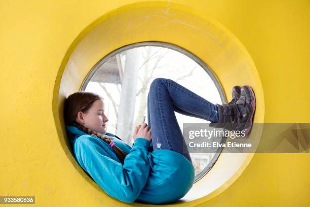 Teenager using mobile phone and lying down with feet up in the frame of a circular window in a yellow wall