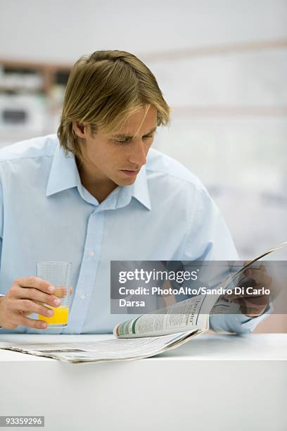 man with glass of juice looking at newspaper - glass magazine stock-fotos und bilder