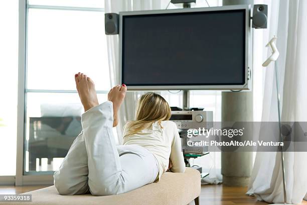 female lying on stomach watching flat screen tv, rear view - flat stomach stock-fotos und bilder