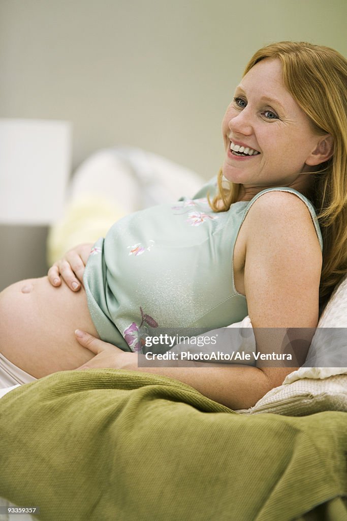 Pregnant woman reclining, hands on bare belly, smiling