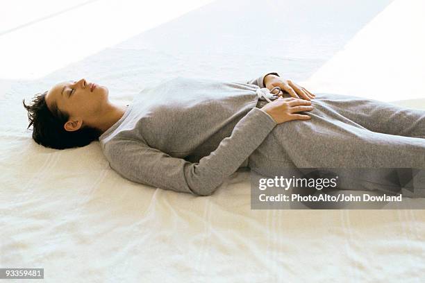 woman wearing athletic wear lying on back with hands placed on lower abdomen - women lying imagens e fotografias de stock