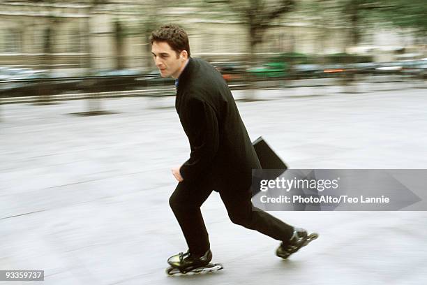 man in business attire inline skating carrying briefcase in city square - speed skating stock-fotos und bilder