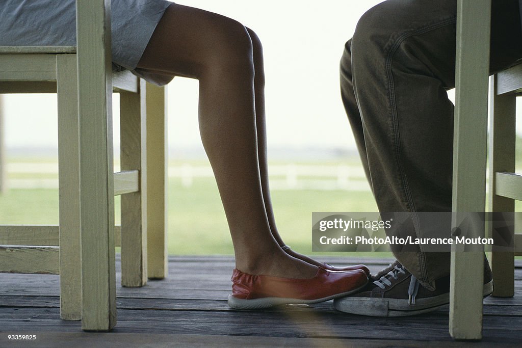 Young couple seated at table facing one another, woman's feet touching mans, low section