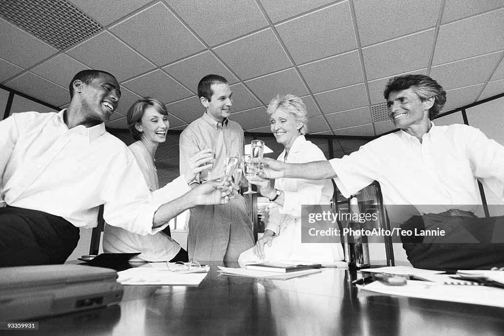 Business associates clinking glasses, celebrating with champagne in office