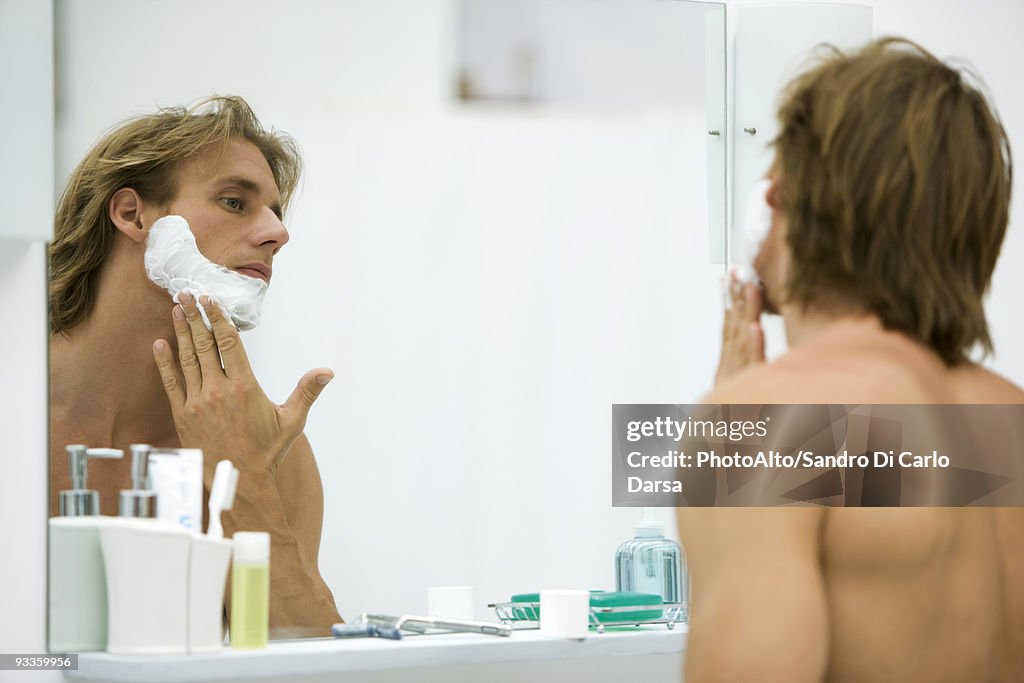 Man applying shaving cream in bathroom mirror