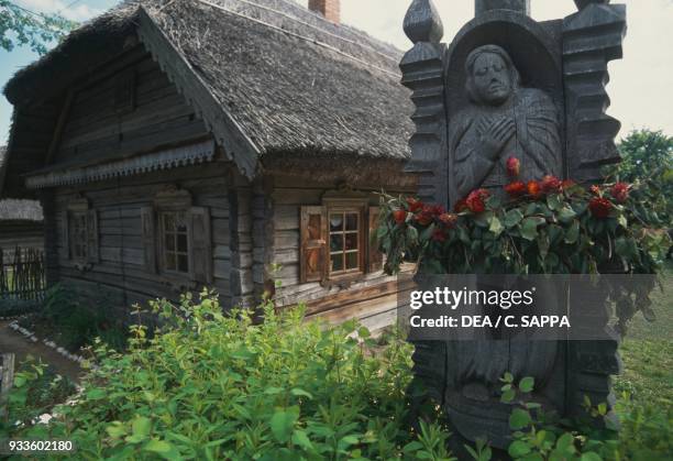 Traditional house with carved wooden statue on the right, open-air museum of Kaunas, Lithuania.