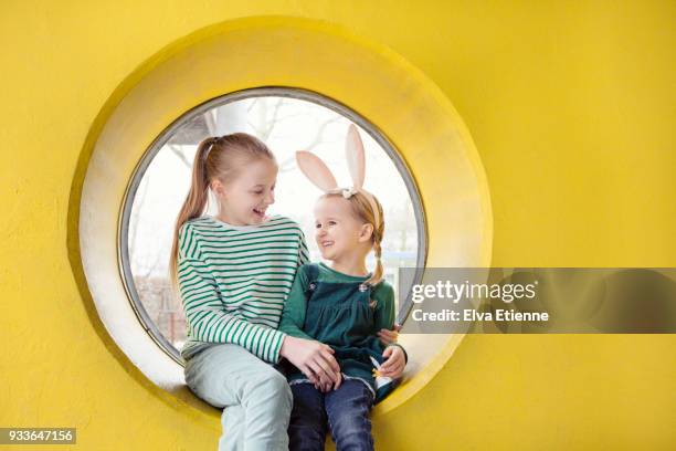 two happy children sitting on the frame of a circular window in a yellow wall - family picture frame stockfoto's en -beelden