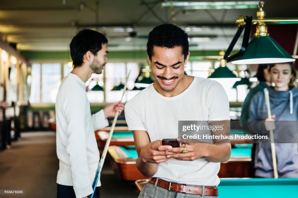 Stylish Young Man Smiling While Using Smartphone At Pool Hall
