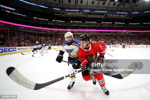 Joel Edmundson of the St. Louis Blues and Alex DeBrincat of the Chicago Blackhawks get physical in the second period at the United Center on March...