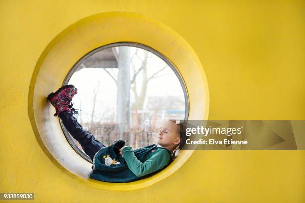 girl (4-5) resting inside a circular window in a yellow wall - bright colour wall stock pictures, royalty-free photos & images