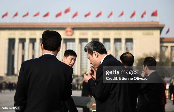 Delegates smoke a cigarette on Tiananmen Square before the seventh plenary session of the 13th National People's Congress at the Great Hall of the...