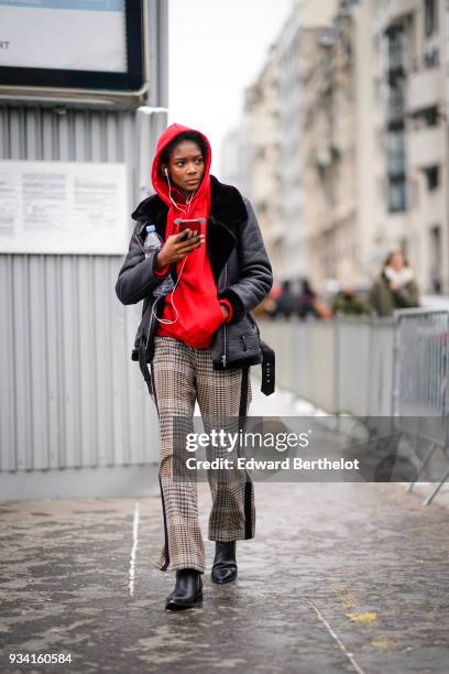 Guest wears a red hooded top, a black sheepskin jacket, brown prince-de-galles checkered pants with a dark brown stripe on the side, black boots,...