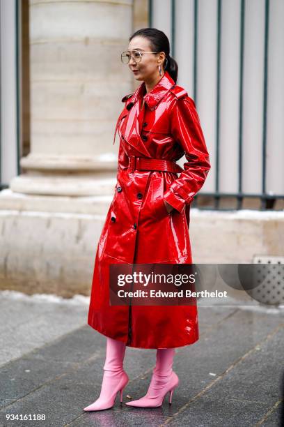 Guest wears large creole earrings, a glossy red vinyl trenchcoat with a back-flap, pink pointy toe high-heeled shoes, during Paris Fashion Week...