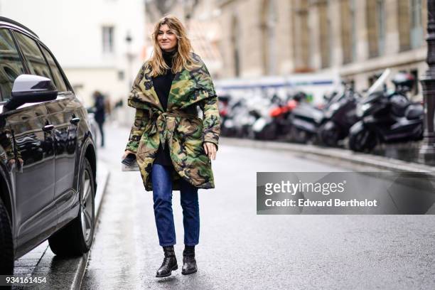 Guest wears a large collar with round edges camouflage puffy coat, a black turtleneck, blue jeans, black lace-up shoes, during Paris Fashion Week...