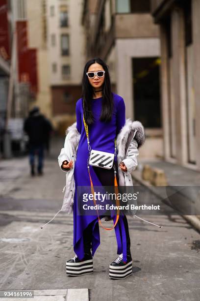 Guest wears white sunglasses, an off-white fur-lined, hooded parka, a deep purple, long, asymmetric and front slit long dress tied by a bow, a black...