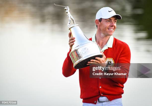 Rory McIlroy of Northern Ireland smiles and holds the tournament trophy while wearing a replica Arnold Palmer red cardigan following his three stroke...