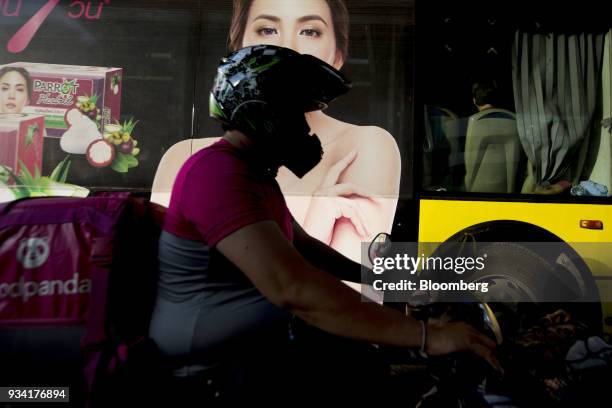 Courier for Foodpanda, a meal-delivery service operated by Delivery Hero AG, rides his motorcycle past a bus in Bangkok, Thailand, on Friday, March...