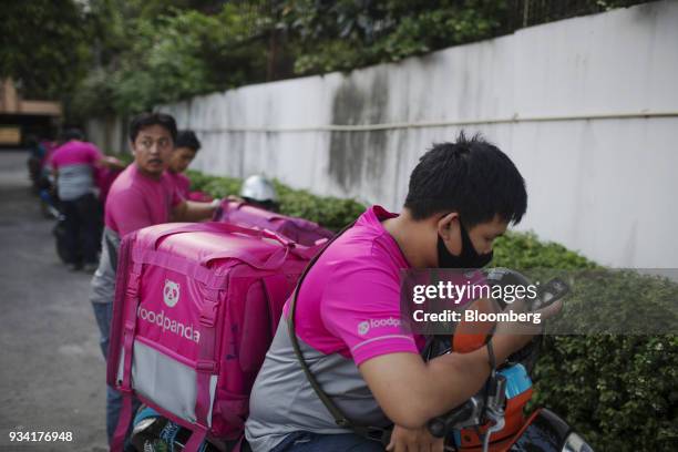 Courier for Foodpanda, a meal-delivery service operated by Delivery Hero AG, checks his smartphone while sitting on a motorcycle at the company's...