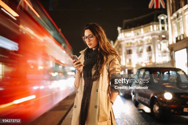 portret van een jonge vrouw op de drukke straten van london centrum in de avond, sms voor een taxi - lange sluitertijd stockfoto's en -beelden
