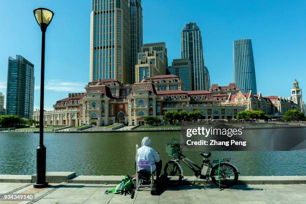 Man sits fishing beside Haihe river, facing Jinwan Plaza, which is the economy and business landmark of the city. In 2017, Tianjin's gross domestic...