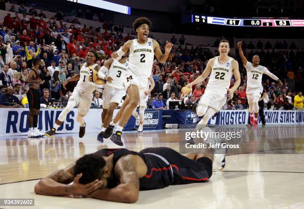 Jordan Poole and teammates of the Michigan Wolverines celebrate Poole's 3-point buzzer beater for a 64-63 win as Devin Davis of the Houston Cougars...