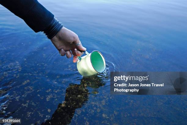 a metal camp cup gets filled with fresh, clear lake water - handvol stockfoto's en -beelden