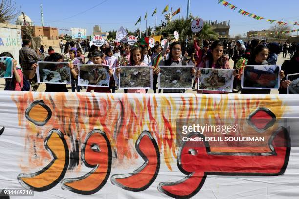 Syrian Kurds hold a banner reading "Noruz" and depicting the new year celebration as bloody and violent, as they take part in a protest in the...