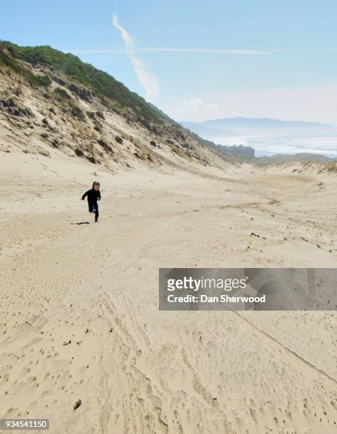 boy running up a sand dune at the beach at cape kiwanda - oregon - dan sherwood photography - fotografias e filmes do acervo