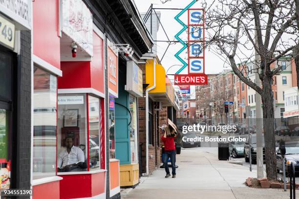 Passersby walk near shops on Broadway in the Winter Hill neighborhood of Somerville, MA on March 6, 2018.