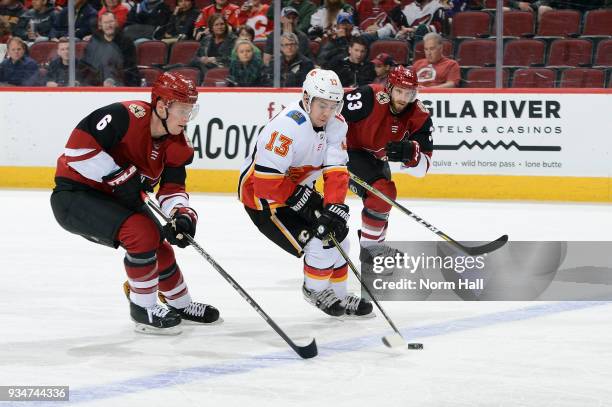 Johnny Gaudreau of the Calgary Flames advances the puck up ice ahead of Jakob Chychrun and Alex Goligoski of the Arizona Coyotes during the first...