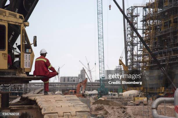 Workers observes a crane being used to lay pipework at a steam cracker unit at the under construction Petronas Nasional Berhad Refinery and...
