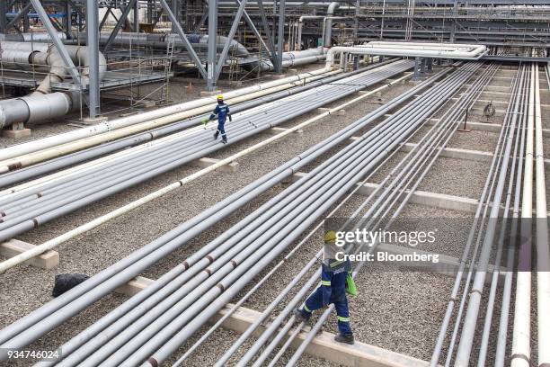 Workers walk over pipework at the under construction Petronas Nasional Berhad Refinery and Petrochemical Integrated Development Project, part of the...