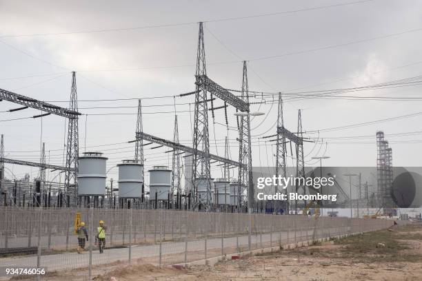 Workers walk along a road as transmission lines run overhead at the under construction Petronas Nasional Berhad Refinery and Petrochemical Integrated...