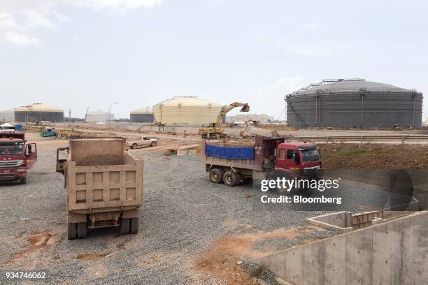 Trucks sit parked as oil tanks stand in the background at the under construction Petronas Nasional Berhad Refinery and Petrochemical Integrated...