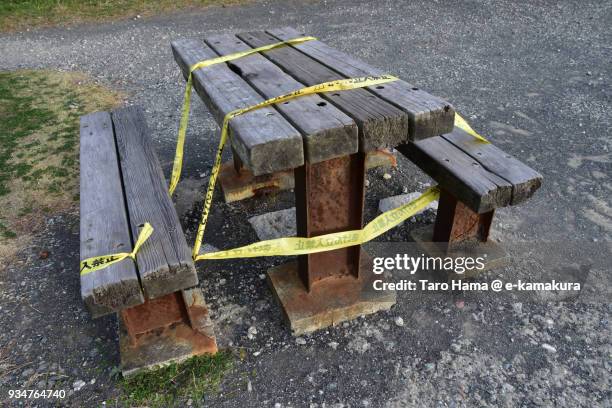 a wooden and steal table and chair broken by long-years' sea breeze and warning yellow-colored tapes in kamakura beach park in kamakura city in kanagawa prefecture in japan - broken chair stock pictures, royalty-free photos & images