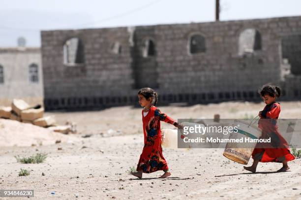 Yemeni little sisters carry jerrycans walk to a water pump to fill it with water on March 18, 2018 in Sana'a, Yemen.