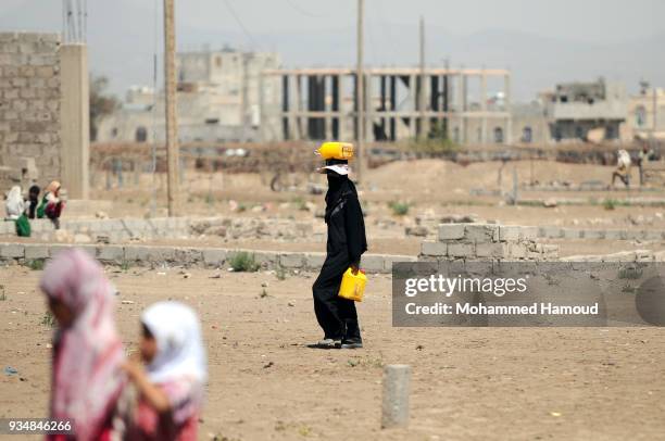 Yemeni woman returns home with jerrycans after she filled it with water on March 18, 2018 in Sana'a, Yemen.