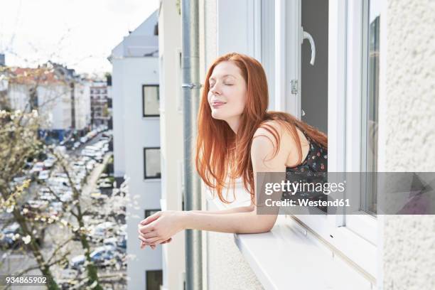 portrait of redheaded woman with eyes closed leaning out of window - leunen stockfoto's en -beelden