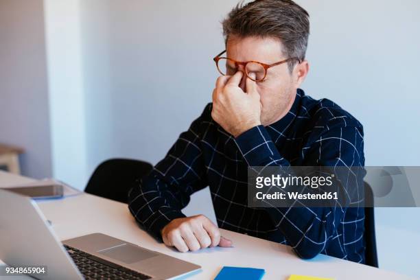 businessman at desk in office rubbing his eyes - frustración fotografías e imágenes de stock