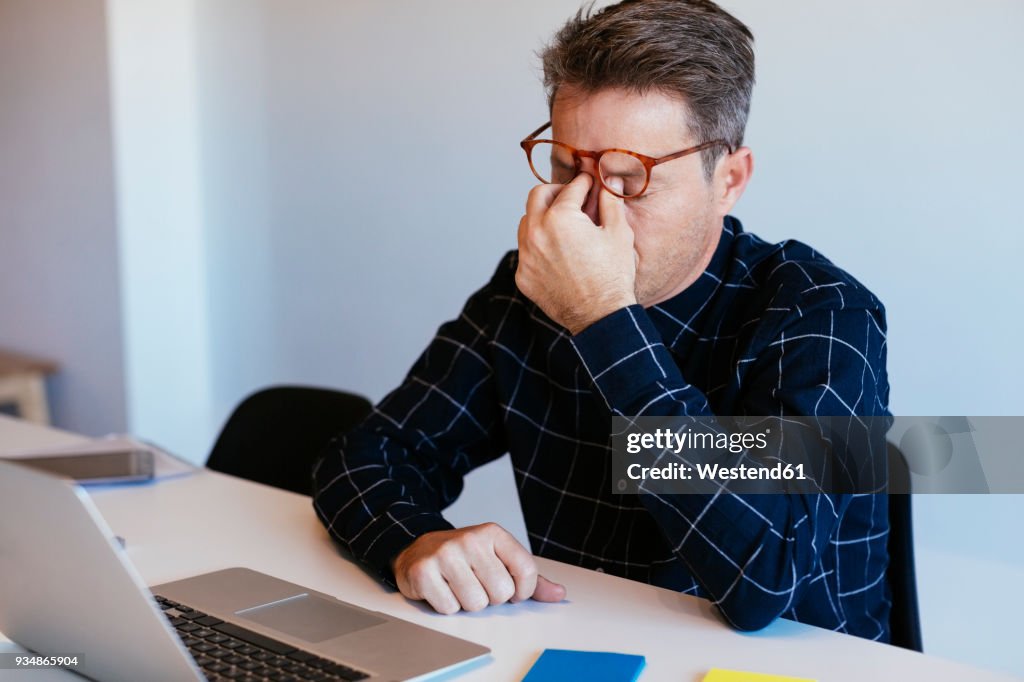 Businessman at desk in office rubbing his eyes