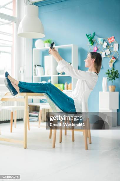 smiling woman with feet up taking selfie in a loft - feet selfie woman stockfoto's en -beelden
