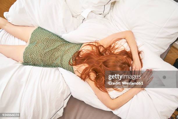 back view of redheaded woman lying on bed - allongé sur le devant photos et images de collection
