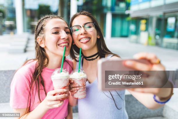 two happy teenage girls drinking milkshakes in the city taking a selfie - girl selfie stock pictures, royalty-free photos & images