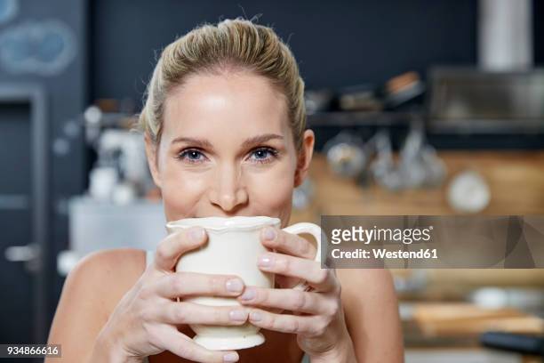 portrait of smiling blond woman in the kitchen holding coffee mug - kaffe trinken stock-fotos und bilder