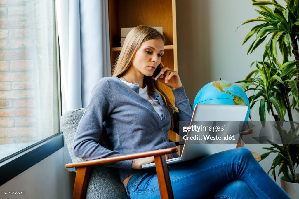 Young woman sitting in arm chair using laptop