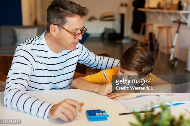 father watching son doing homework at table - workbook stock pictures, royalty-free photos & images