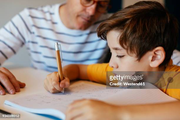 father watching son doing homework at table - genderblend stock-fotos und bilder